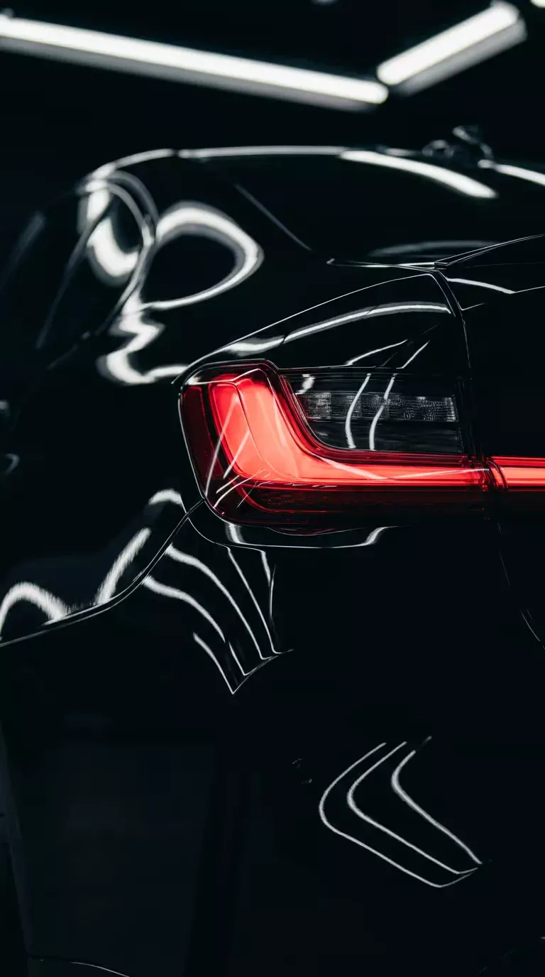 Mirror-finish black paint reflecting studio lights beside a red tail light